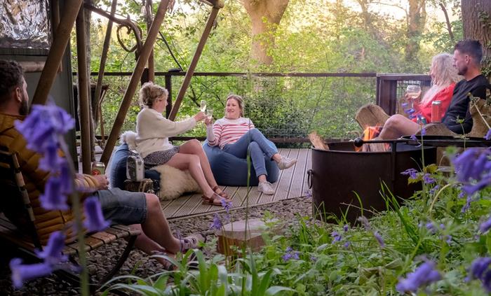 Group of friends around a firepit on the deck of safari tent in the woods at Hay-on-Wye, Wales.  Bluebells